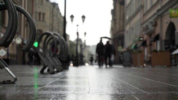 雨后的城市街道一群人在雨中打着雨伞沿着潮湿光亮的人行道上下班水坑里映出人影的影子秋天在夏日的雨中模糊城市街道上的雨天背景实时