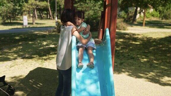 小女孩抱着妈妈站在公园的滑梯上