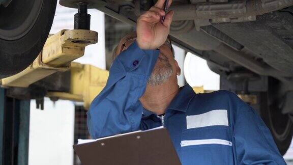资深亚洲汽车技工在车下用夹板检查并在车库里用扳手修理老亚洲汽车修理工工作