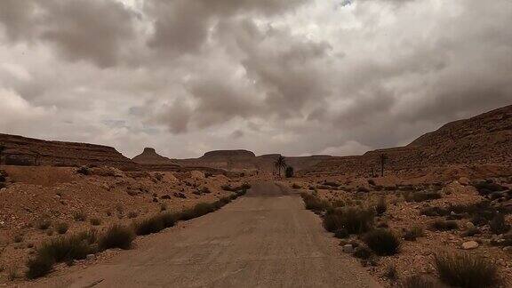 在阴天的背景中开车在突尼斯的沙漠道路上与KsarGuermessa穴居人村庄司机的观点