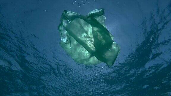 慢镜头绿色的塑料袋在阳光的照射下缓缓地漂浮在水下表面海洋的塑料污染水下拍摄低角度拍摄背光拍摄