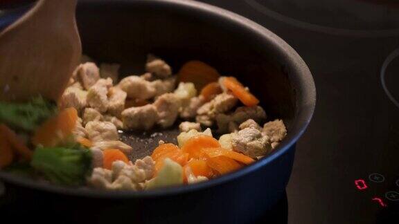在一个黑色煎锅里烹饪蔬菜和鸡肉站在一个触摸敏感的铁架上准备健康晚餐煎胡萝卜花椰菜花椰菜和白鸡肉