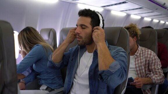 英俊的男子选择播放列表戴上耳机闭上眼睛在飞机上看起来很放松
