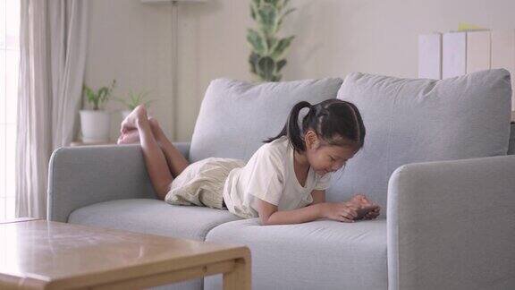 快乐的小女孩躺在客厅的沙发上玩智能手机游戏