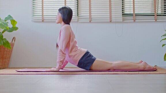 健康迷人的亚洲女性在休闲做瑜伽Cobra姿势在家里冥想舒适和放松冷静的健康年轻女性深呼吸和冥想与瑜伽在家里瑜伽概念