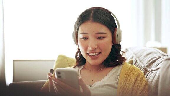 手机放松或女孩戴着耳机在社交媒体上阅读在线内容在八卦博客网站在家里移动应用程序音频音乐或快乐的亚洲女性搜索互联网视频或有趣的播客帖子