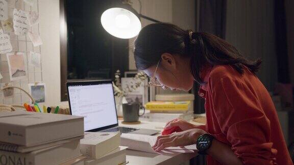 年轻的亚洲女性穿着休闲拿着笔记本电脑坐在桌子前晚上在家里的客厅里思考创作工作想法居家办公