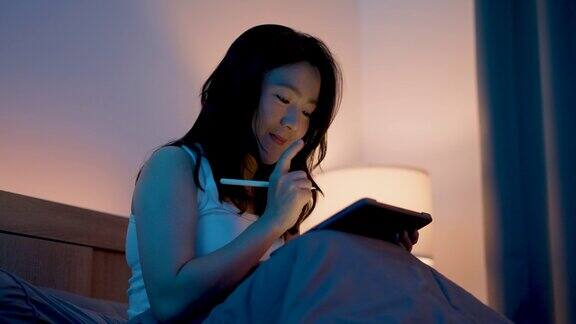 亚洲女性晚上坐在卧室里用智能铅笔在数字平板电脑屏幕上画画