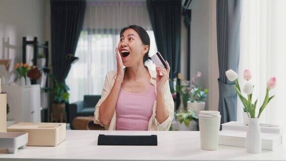 年轻的亚洲女女孩穿着休闲坐在书桌前与数字平板电脑和信用卡感到兴奋和快乐在网上购物成功支付在客厅在家里