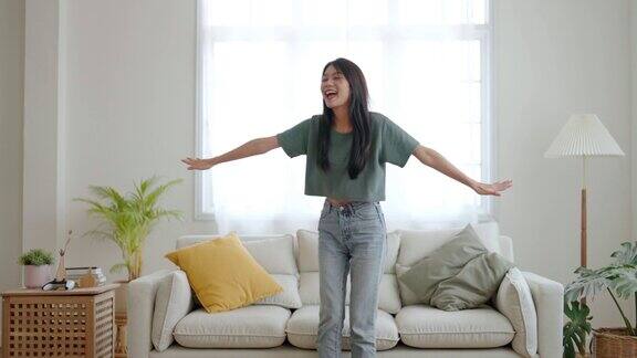 年轻的亚洲女人在家里客厅的地板上跳舞快乐的亚洲女性微笑放松在家里健康的精神健康和幸福