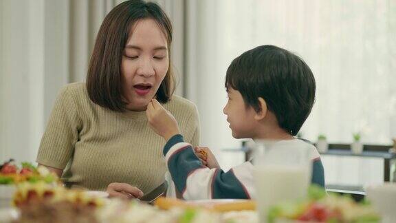 幸福的亚洲家庭年轻美丽的妈妈和她可爱的小儿子在家里的餐厅一起享用早餐6岁的儿子正在给他妈妈吃薯片享受在家吃饭与家人共度美好时光