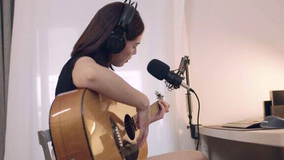 美丽的年轻亚洲妇女学习弹吉他和唱歌在家工作室