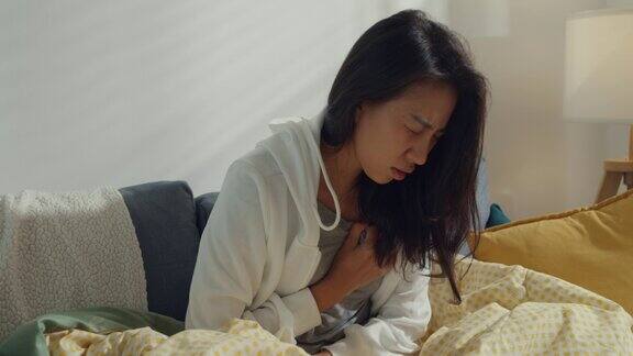 生病的年轻亚洲妇女心脏病发作坐在家里客厅的沙发上
