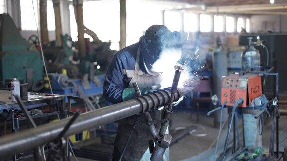 在冶金工厂穿着蓝色工作服戴着防护面具的男工人通过电焊连接金属元件重工业工人在室内用角磨机切割钢材