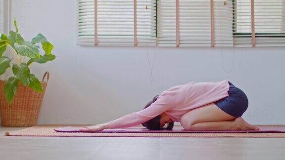 亚洲妇女在休闲做瑜伽锻炼瑜伽儿童姿势或Balasana平静的健康年轻女性呼吸和冥想与瑜伽在家里锻炼为健康的生活
