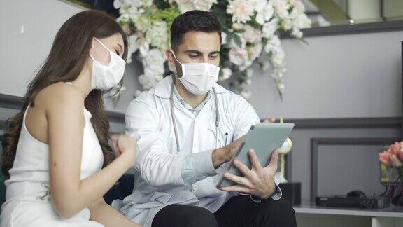 戴着口罩的4K男医生在医院用数码平板电脑与女患者交谈