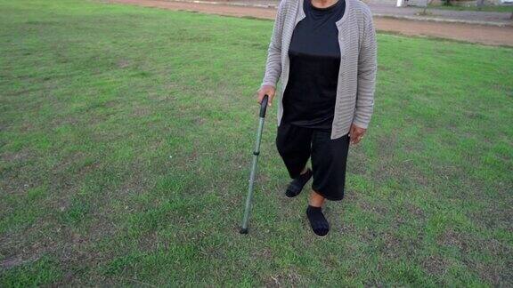 老妇人拄着拐杖在草地上慢步行走