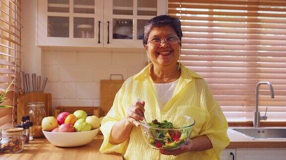亚洲老年妇女在家里拿着一碗蔬菜的肖像有魅力的成熟老人长辈系着围裙闲暇时在家做饭养生饮食和健康食品