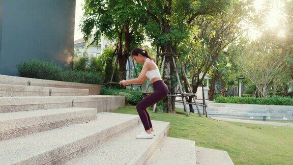 美丽年轻的亚洲运动员女士锻炼做深蹲跳跃后在公园环境在傍晚日落在城市楼梯上跑步