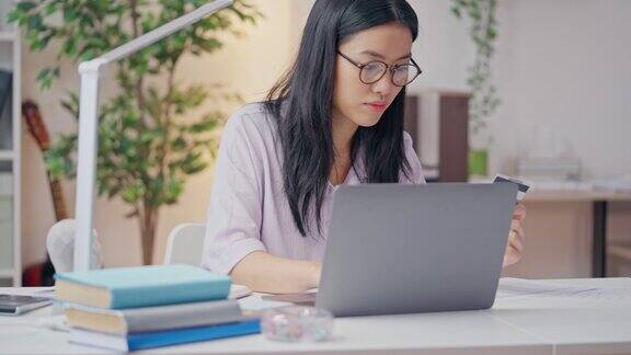 戴眼镜的年轻女子在笔记本电脑上插入信用卡号码在网上购物