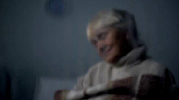可怜的老妇人睡在疗养院下雨的窗户后面的椅子上