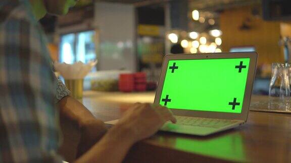 男人用绿色屏幕的显示器敲击笔记本电脑的键盘