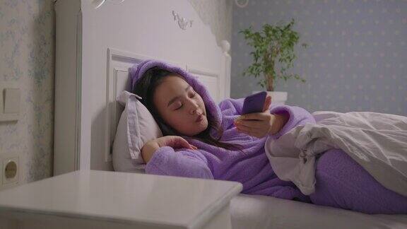 一个穿着紫色睡衣的亚洲女人醒来后手里拿着手机躺在床上睡眼惺忪的女人早上还在用手机