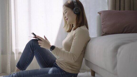 年轻的亚洲妇女在家里休息的时候用平板电脑听音乐