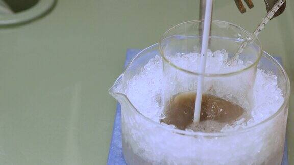 搅拌在烧杯中的化学溶液同时用温度计在冰中冷却