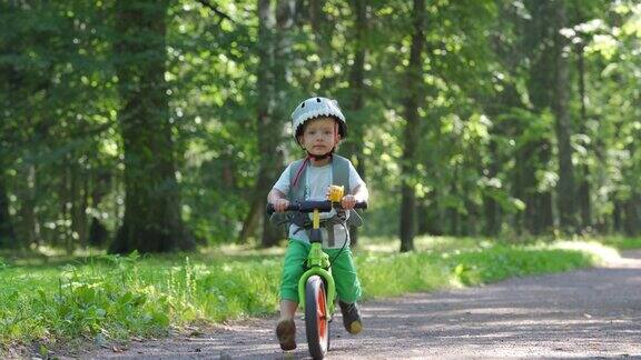 蹒跚学步的孩子戴着保护头盔在夏季公园骑平衡自行车