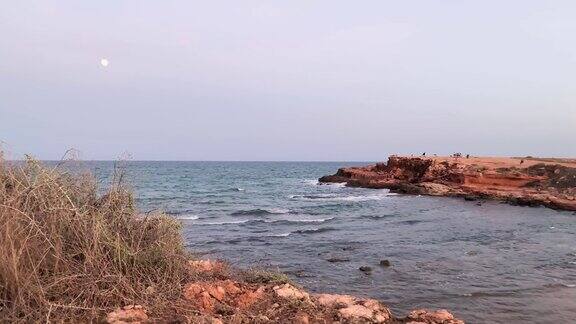 地中海沿岸的植被背景是大海和月亮暴风雨来临之前日落时分的小海湾和风景如画的海滩地中海岩石海岸的红色斜坡波浪拍打着岩石海岸版本4