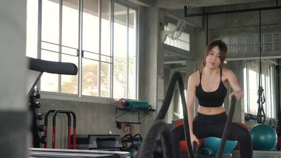 女子在健身房用格斗绳训练强大迷人的亚洲女人做战斗训练与绳子在健身房在慢动作