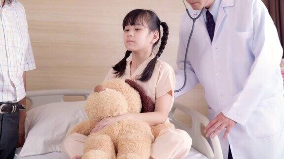 医生在医院病房探望小女孩病人并使用听诊器从背部听肺呼吸作为日常工作医院保健理念