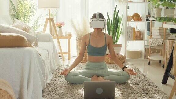 年轻的亚洲运动女性戴着虚拟现实头盔运动上衣和紧身裤在家里的客厅练习瑜伽饮食和健康减肥