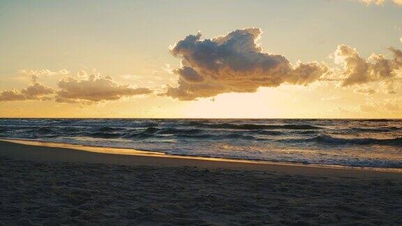 日落在海浪和沙滩上的云后面