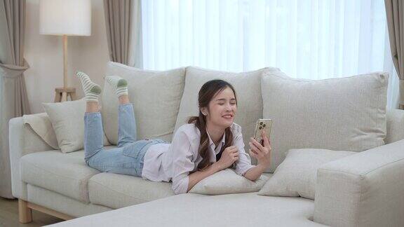 快乐的亚洲女人在家里的客厅用智能手机和朋友视频聊天