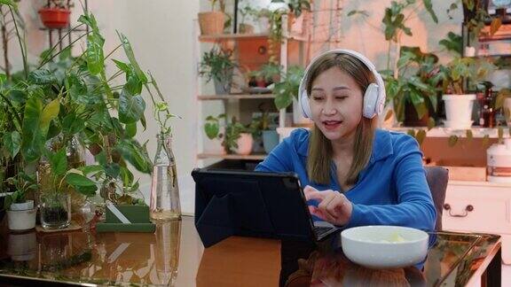 年轻的亚洲女性在家使用笔记本电脑工作时戴着无线耳机