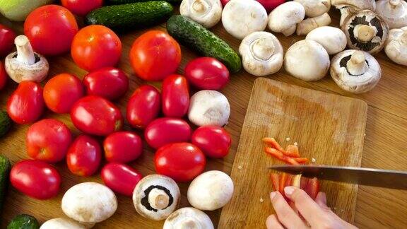 女人的手正在厨房桌子上的木板上切红辣椒和蔬菜