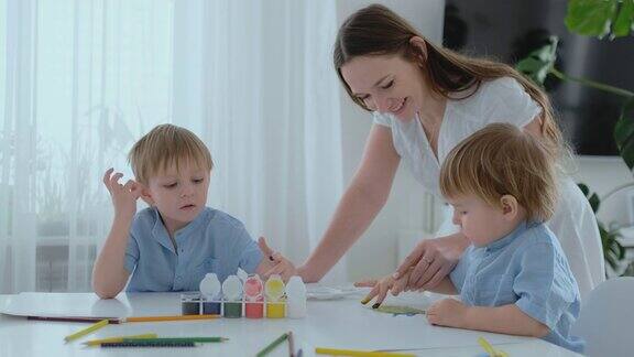 妈妈帮助她的儿子发展创造性技能并参与他们用手指创造绘画颜料孩子的发展创造性的家庭爱的妈妈