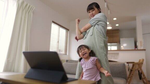 妈妈和小女儿在家里用平板电脑看电影跳舞