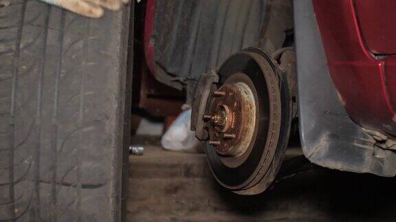 这个人拧下了汽车上的轮子把它从车库里的汽车里取出来一个男人自己在他的车库里给他的车换刹车盘更换汽车刹车盘