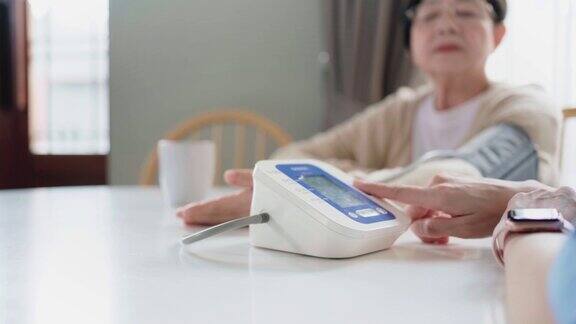 护士按下亚洲老年妇女的自动血压计按钮测量血压照顾者的访问家庭健康护理和养老院慢动作4k视频