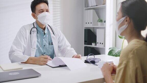 成熟的亚洲男性医生在健康门诊咨询女性患者时佩戴防护口罩
