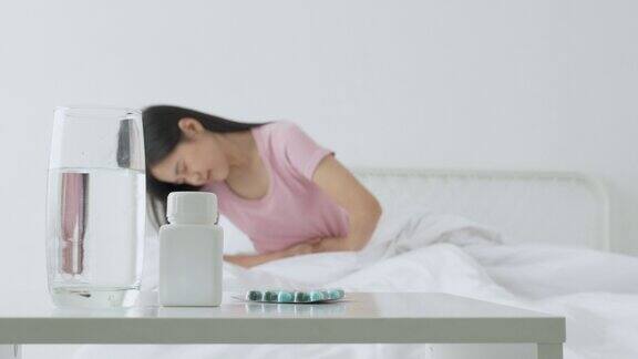 年轻亚洲女性坐在床上腹痛或肠病便秘或消化不良在家卧室不快乐女性生病和月经和胃痛医学和健康观念