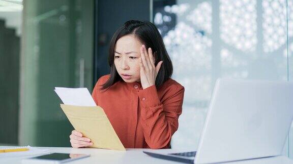 悲伤的亚洲妇女坐在现代办公室的工作场所读着带坏消息的信