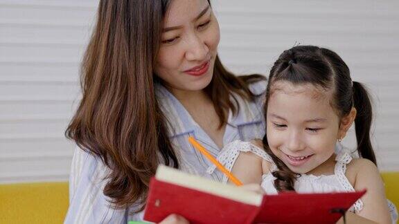 女儿和母亲坐在公寓的客厅里看书微笑着玩幼儿喜欢家庭写作活动照顾幼儿学习幸福的家庭生活方式