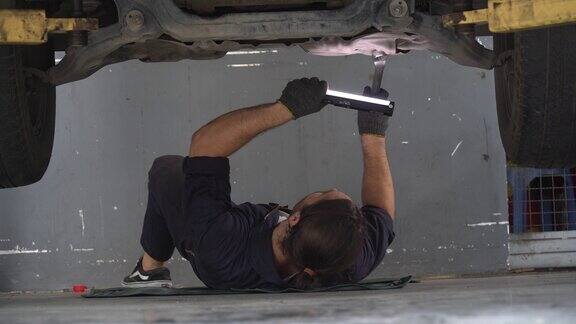 汽车修理工躺在车下检查用扳手和手电筒修理汽车修理厂汽车修理工工作