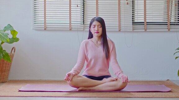 平静的健康亚洲年轻女性坐在地毯上呼吸瑜伽莲花姿势瑜伽冥想年轻健康女性放松和舒适的白色舒适的家瑜伽锻炼为健康