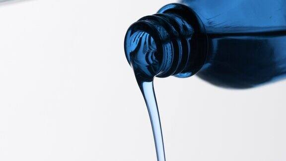 蓝色的唐茜油从蓝色的瓶子倒在灰色的背景