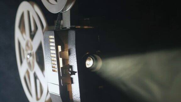 一个老式的古董超级8毫米电影放映机的正面视图投射一束光在一个黑暗的房间旁边的一堆散开的电影